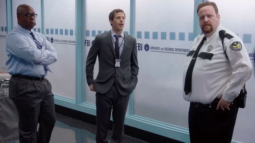 Captain Holt (Andre Braugher) and Jake Peralta (Andy Samberg) attempt to sneak a crucial FBI file past Phil (Ben Zelevan